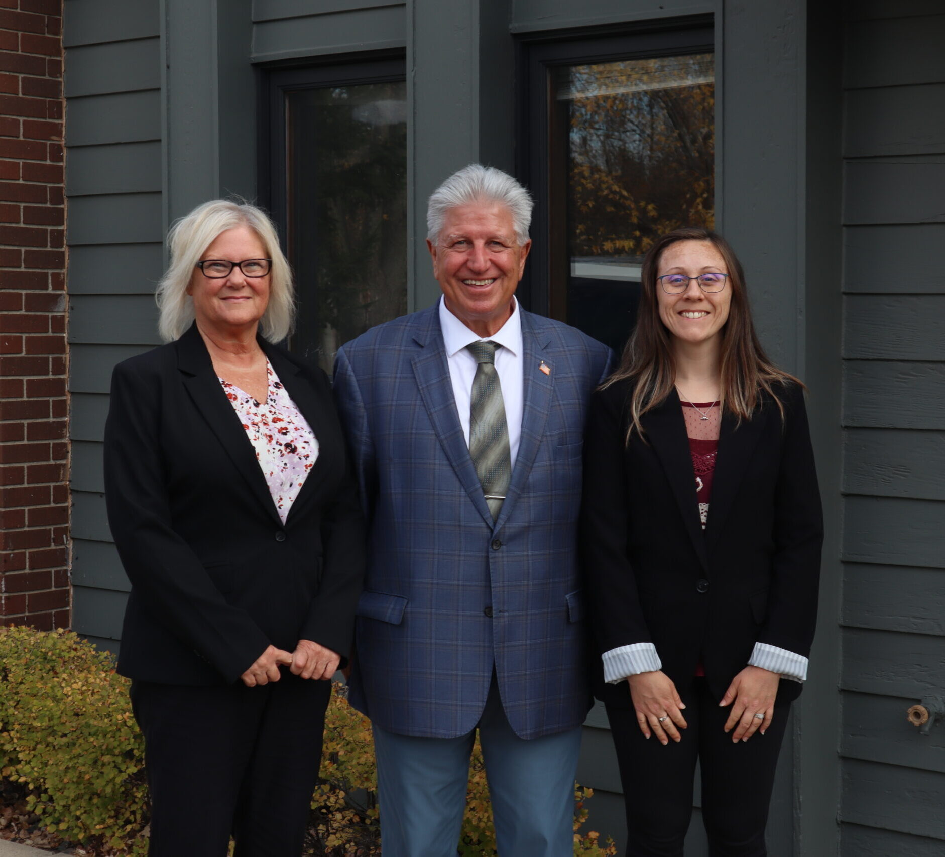 A man in a suit and two women in blazers standing together outside a building.